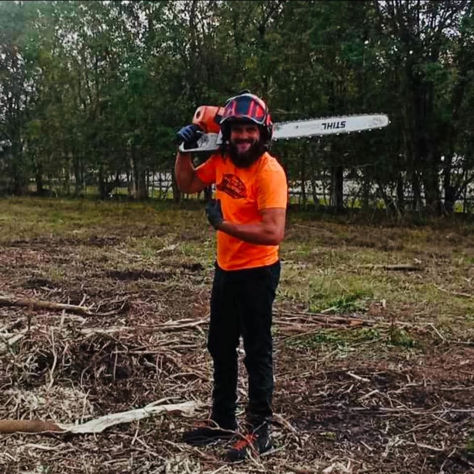 Erik Thorne on a freshly cleared job site holding a Stihl chainsaw, wearing safety helmet and orange Thorne Works shirt